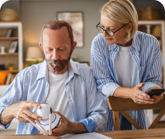 Der Mann und die Frau betrachten gemeinsam eine Smart Home Kamera. Die Frau hält ein Smartphone in der Hand.